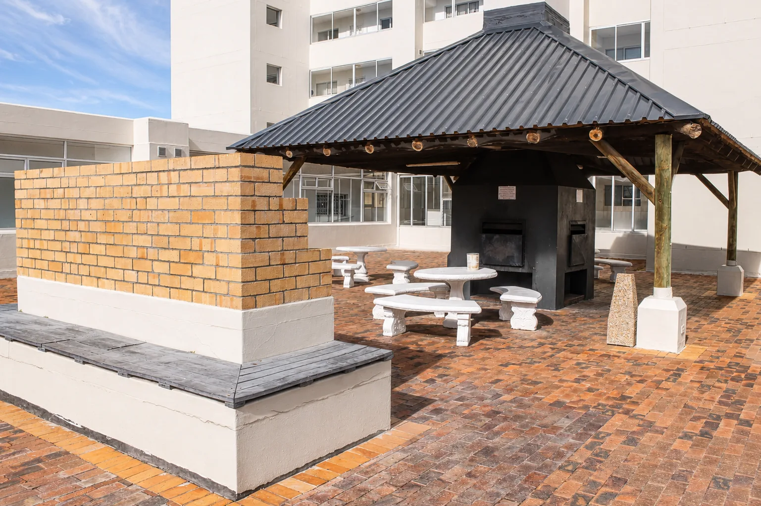 Brick-paved apartment courtyard with a covered communal braai and outdoor seating