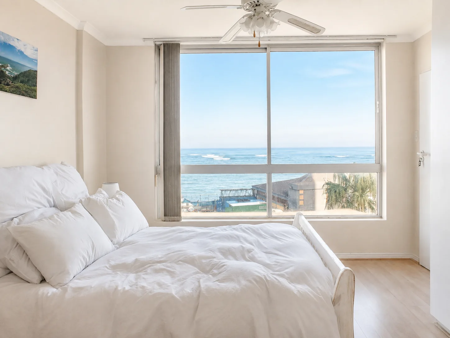 Light-filled bedroom with white bedding and a wide panoramic view across the ocean