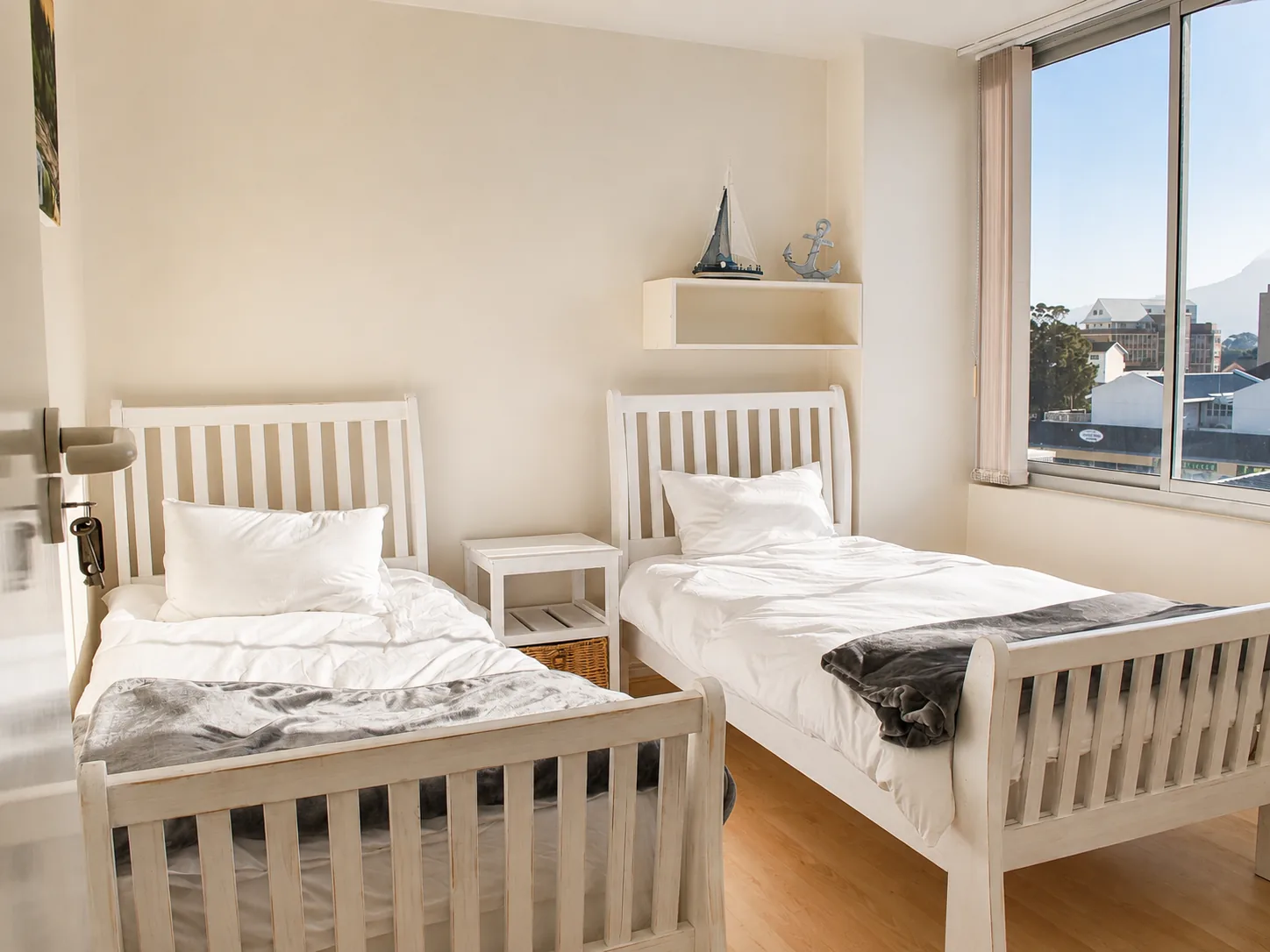 Bright twin bedroom with two white single beds, grey throws and a large window with a mountain view