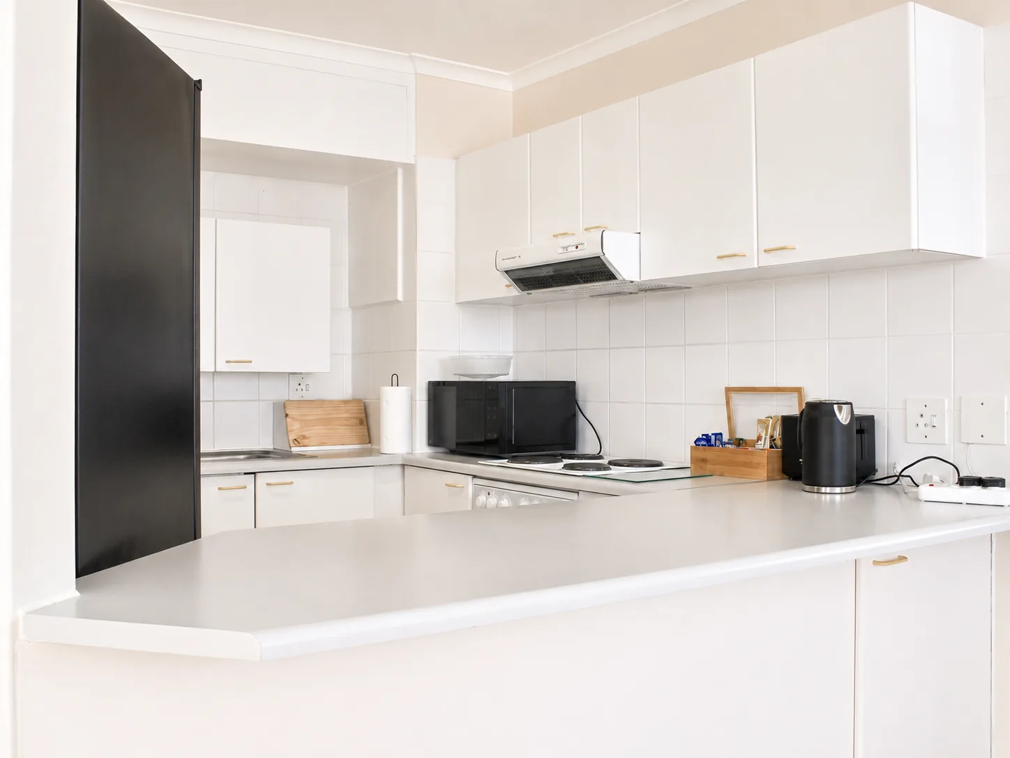 Bright self-catering kitchen with white cabinets, breakfast counter, fridge, oven, microwave and kettle