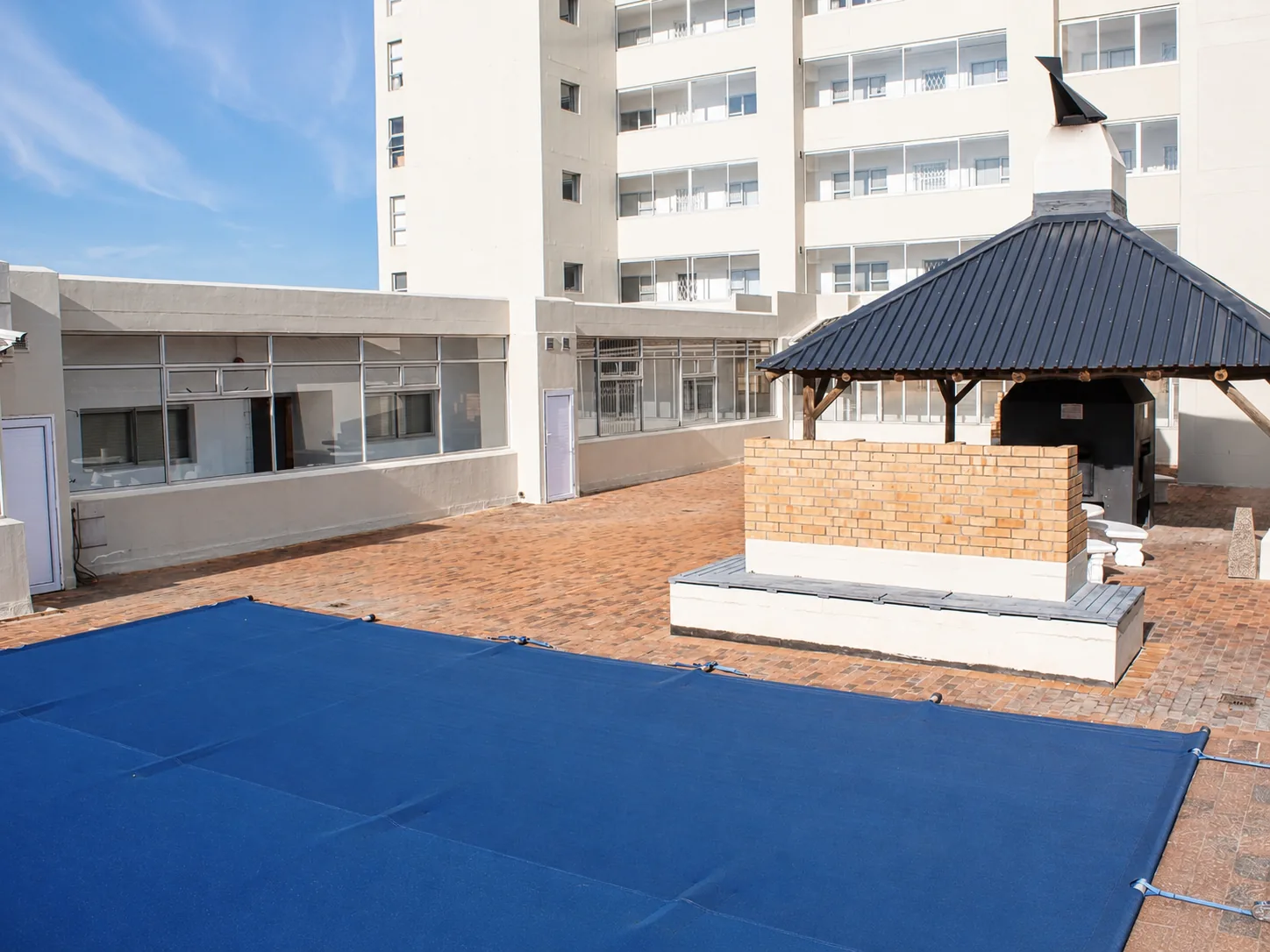 Apartment courtyard featuring a blue-covered swimming pool and covered communal braai area