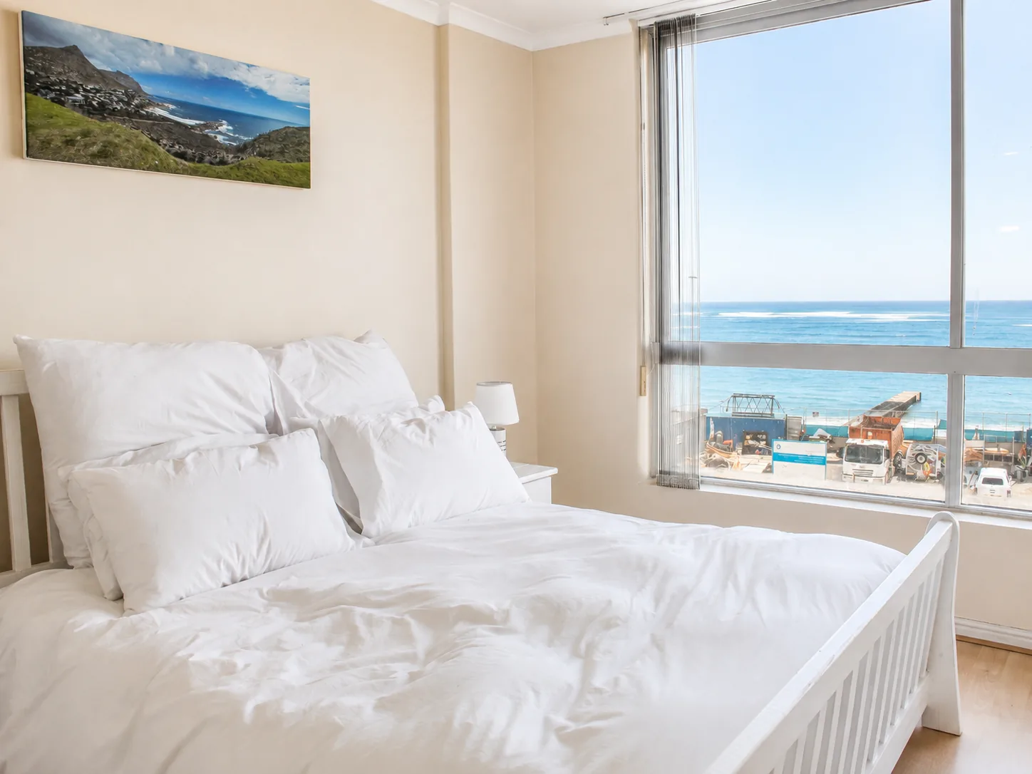 Comfortable double bedroom with white bedding and a large window overlooking the ocean