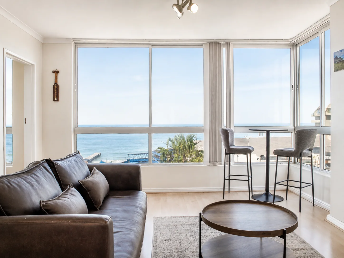 Bright living room with a leather sofa, round coffee table and window-side breakfast table overlooking the ocean