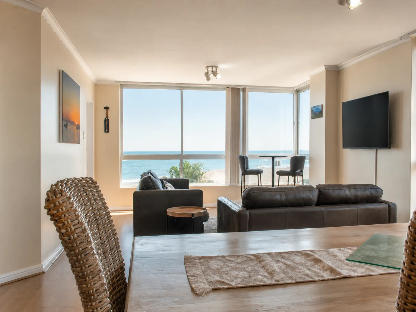 Open-plan dining and living room with leather sofas, television and large windows overlooking the ocean