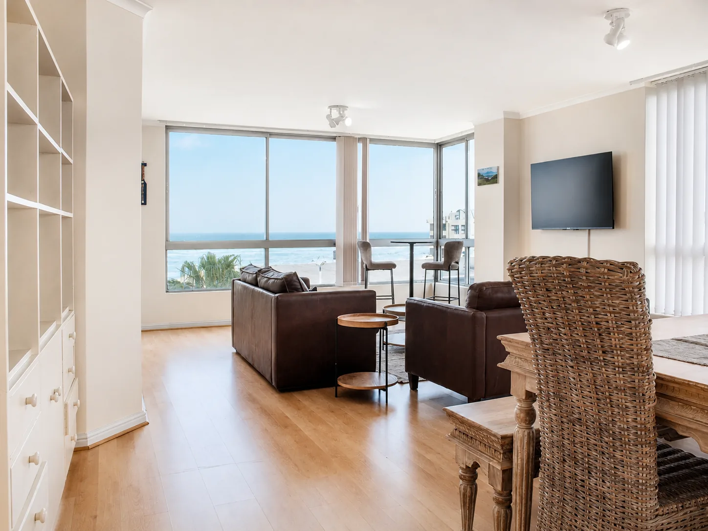 Spacious open-plan living and dining area with leather seating, wicker chairs and large ocean-facing windows